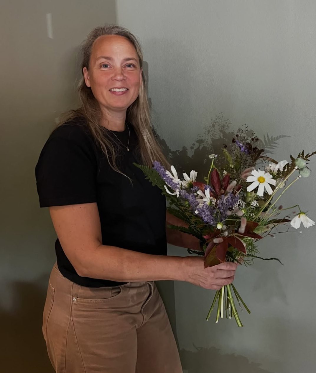 Maria Lithell Bergström, grundare av Tant Bergs Blomaffär, håller upp en handplockad sommarbukett och ler.